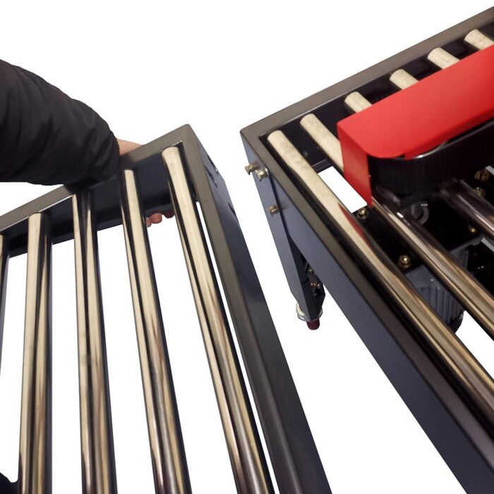 Ręka reguluje metalowy przenośnik rolkowy w pobliżu innego z czerwoną częścią, prawdopodobnie do integracji z Półautomatyczną zaklejarką Easy Tape 70 TSB, obie na białym tle.