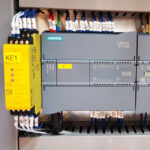 Zbliżenie elektrycznego panelu sterowania przedstawiającego sterownik PLC Siemens SIMATIC S7-1200 podłączony do Automatycznej Formierki Prędkości 50 SB TN HM, z żółtym przekaźnikiem bezpieczeństwa Pilz KE1 widocznym po lewej stronie.