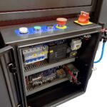 Otwarty przemysłowy panel sterowania z przyciskami, przełącznikami, wyłącznikiem awaryjnym oraz starannie rozmieszczonymi wyłącznikami i przekaźnikami - idealny do automatycznej zaklejarki Auto Tape 50 HM.