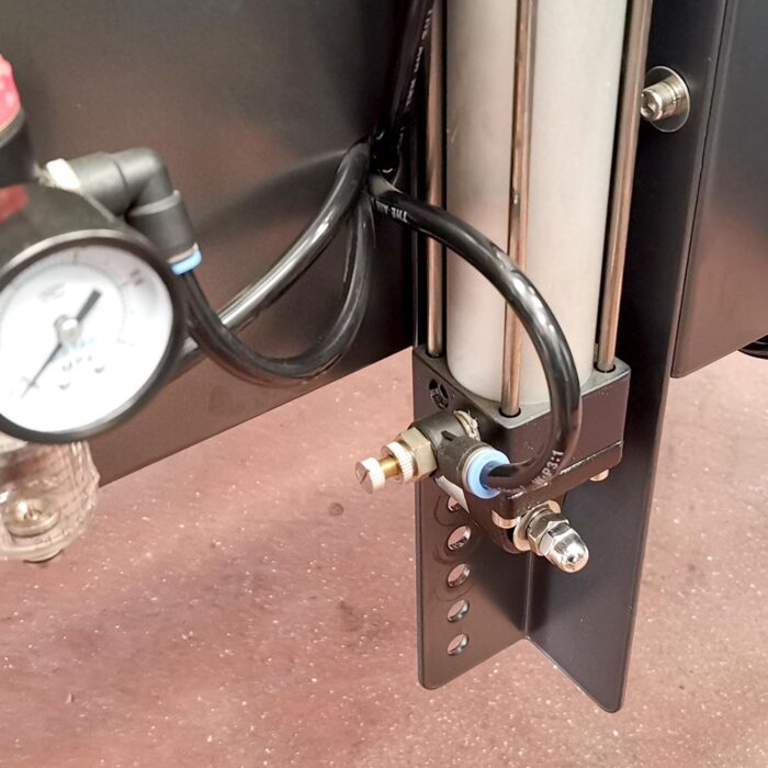 Zbliżenie układu pneumatycznego z metalowym cylindrem, rurkami i manometrem - kluczowymi elementami Półautomatycznej zaklejarki Random Tape 50 SB - bezpiecznie zamontowanymi za pomocą śrub i łączników na brązowej powierzchni.