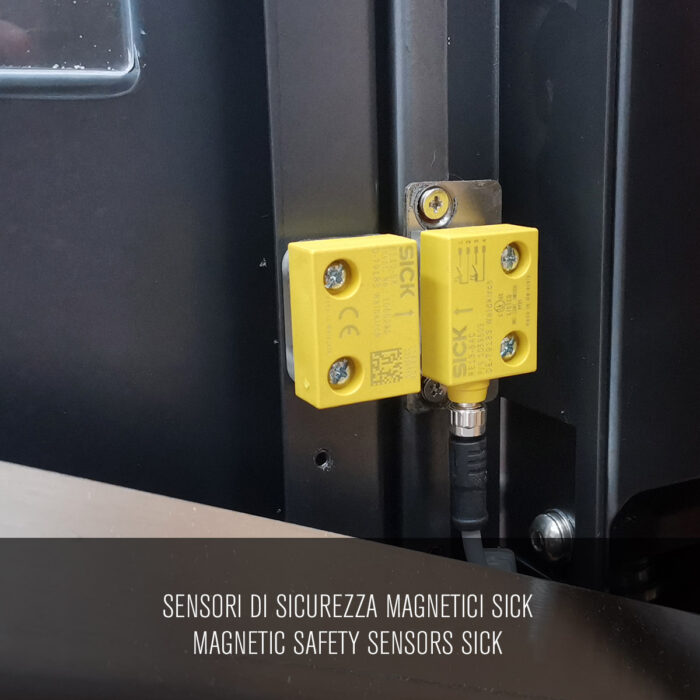 Dwa żółte magnetyczne czujniki bezpieczeństwa SICK są zamontowane na czarnej metalowej powierzchni Automatycznej Formierki Prędkości 50 SB TN. Tekst poniżej brzmi: Sensori di sicurezza magnetici SICK / Magnetyczne czujniki bezpieczeństwa SICK.