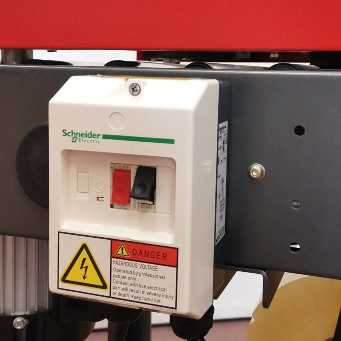 Skrzynka rozdzielcza Schneider Electric z czerwonym przełącznikiem ON/OFF, zielonym wskaźnikiem i żółtym ostrzeżeniem o napięciu jest zamontowana na szarej ramie Półautomatycznej zaklejarki Small Tape 50 SB.