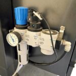 Zbliżenie regulatora ciśnienia powietrza Festo z niebieskim pokrętłem regulacji, manometrem i przewodami na Automatycznej formierce Speed Former 50 SB Servo, pokazujące strzałki kierunkowe i widoczne oznakowanie.