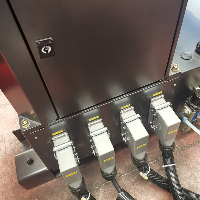 Zbliżenie przemysłowego panelu elektrycznego z czterema szarymi złączami zasilania oznaczonymi żółtymi etykietami i czarnymi kablami na metalowej podstawie - część Automatyczna owijarka palety Techno Wrap 2000 BD.