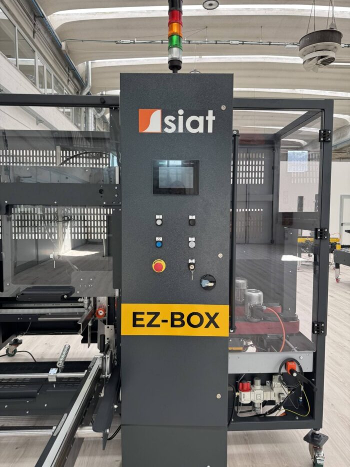 Zbliżenie automatycznej kartoniarki SIAT EZ-BOX XL pokazuje jej ekran, kolorowe przyciski sterujące i wyłącznik awaryjny w ustawieniu fabrycznym.