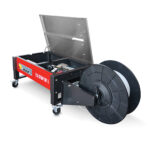 Czerwono-czarna Półautomatyczna bandownica stołowa Eco Strap 501L jest pokazana z otwartą pokrywą, ukazującą wewnętrzne części. Posiada kółka zapewniające mobilność i duży, czarny bęben na taśmę zamontowany z boku.