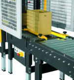 Pudełko kartonowe porusza się wzdłuż metalowego przenośnika rolkowego z osłonami bezpieczeństwa i SIAT SM11 - automatyczną zaklejarką kartonów widoczną w pobliżu panelu sterowania z boku.