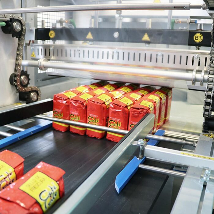 Czerwone paczki kawy przesuwają się wzdłuż przenośnika taśmowego, gdy Automatyczna zgrzewarka do zgrzewek FA800AS owija je i zgrzewa podczas zautomatyzowanego procesu pakowania w fabryce.