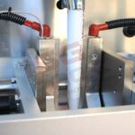 Zbliżenie białej rury zabezpieczonej metalowymi zaciskami z dołączonymi czerwonymi i czarnymi przewodami, pokazanej jako część systemu pakowania Pionowa maszyna pakująca Mini Vert 240 PP.