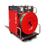 Półautomatyczna bandownica do palet Pallet Strap T150 to czerwono-czarna przemysłowa maszyna do wiązania taśmą wyposażona w dużą zieloną rolkę taśmy z tworzywa sztucznego, panel sterowania, metalowe uchwyty i kółka zapewniające mobilność.