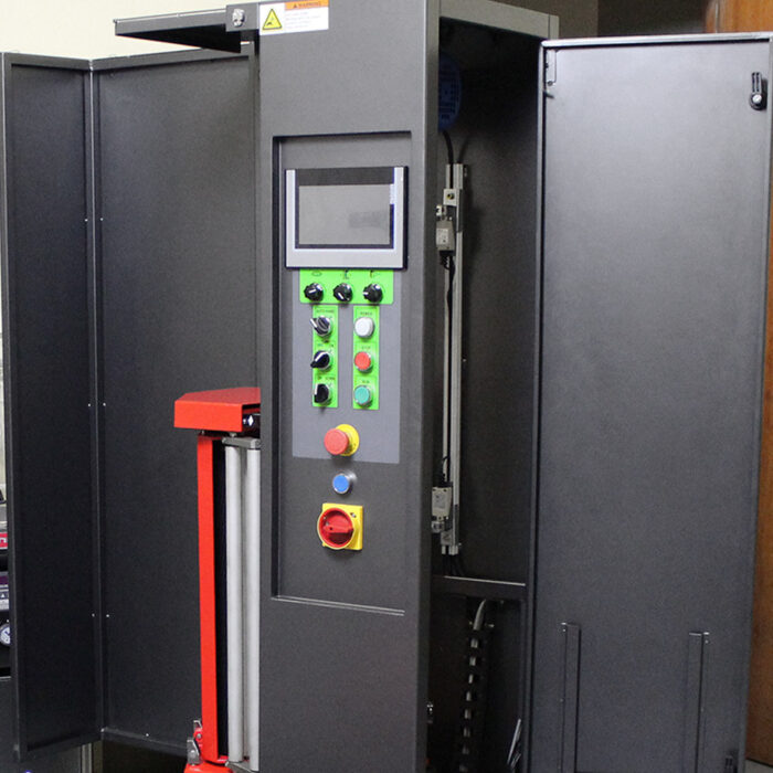 Maszyna przemysłowa Owijarka do walizek Baggy Wrap 900 B posiada otwarte czarne metalowe drzwi, panel sterowania z ekranem dotykowym, przełączniki, kolorowe przyciski (w tym wyłącznik awaryjny) oraz widoczne czerwone i srebrne elementy wewnątrz obudowy.