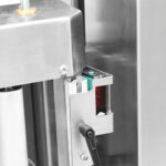 Zbliżenie na Półautomatyczną owijarkę palet Easy Wrap 2000 A SS, maszynę przemysłową ze stali nierdzewnej wyposażoną w czujnik elektroniczny, dźwignię, części mechaniczne i wyraźną czerwoną lampkę kontrolną.