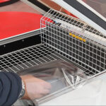 Ręka nosząca zegarek umieszcza lub wyjmuje zapakowany w folię przedmiot na metalowej siatce wewnątrz Zgrzewarki kloszowej do folii Easy Sealer 85.