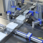 Zbliżenie na Automat pakujący poziomy FLOWPACK SBM750S, wyposażony w metalowe i niebieskie części, owijający prostokątne produkty w przezroczystą folię z tworzywa sztucznego na linii produkcyjnej.