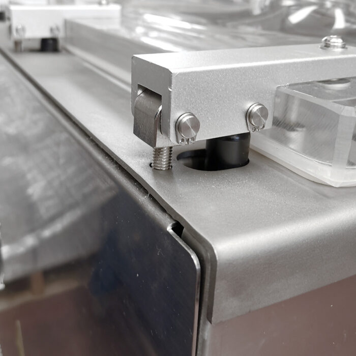 Zbliżenie na Przemysłową pakowarkę próżniową Easy Vac 600S FT pokazuje metalową część maszyny ze śrubami, wystającą śrubę i przezroczysty plastikowy element, a wszystko to na szczotkowanym metalu - podkreślając szczegółowy montaż produktu.