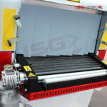 Zbliżenie na metalowe rolki i etykiety ostrzegawcze przemysłowej maszyny pakującej, przedstawiające Tunel obkurczający S 85 DC. Logo ISG PACK jest widoczne w prawym górnym rogu.