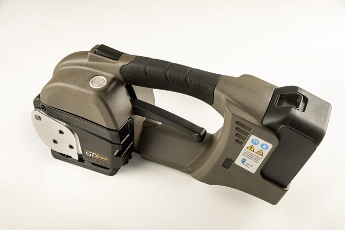 GT-XTREME akumulatorowa wiązarka do taśm PP i PET ma czarno-szarą ręczną konstrukcję z ergonomicznym uchwytem, przyciskami sterującymi i etykietami bezpieczeństwa, pokazanymi na białym tle.