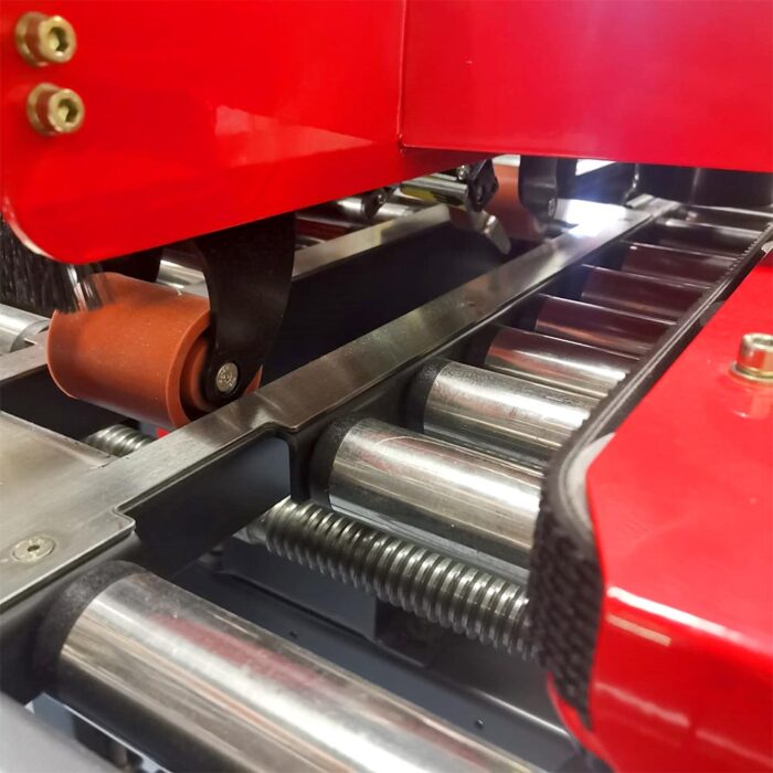 Zbliżenie na półautomatyczną zaklejarkę Small Tape 50 SB, podkreślające jej czerwony korpus, metalowe rolki i sprężyny. Obraz koncentruje się na ruchomych częściach mechanicznych niezbędnych do pakowania lub przenoszenia.