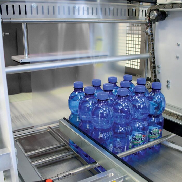 Paczka dwunastu niebieskich plastikowych butelek na wodę Pineta jest bezpiecznie owijana przezroczystą folią przez Automatyczną zgrzewarkę do zgrzewek FA800AS, zapewniając wydajne pakowanie.