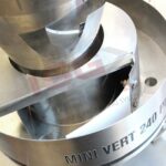 Zbliżenie na Pionową maszynę pakującą Mini Vert 240 PP, pokazujące jej konstrukcję ze stali nierdzewnej i etykietę, z częścią logo widoczną w tle, wskazującą na jej rolę w automatycznych systemach pakowania.