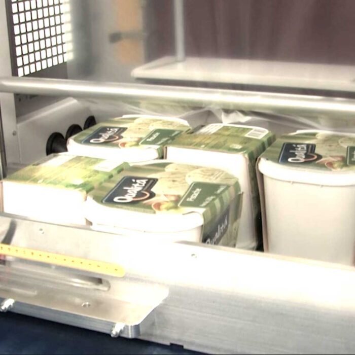 Zbliżenie kilku opakowań sera Quark na linii produkcyjnej, częściowo pokrytych przezroczystą folią wewnątrz Automatycznej zgrzewarki do zgrzewek FA800AR-350P.