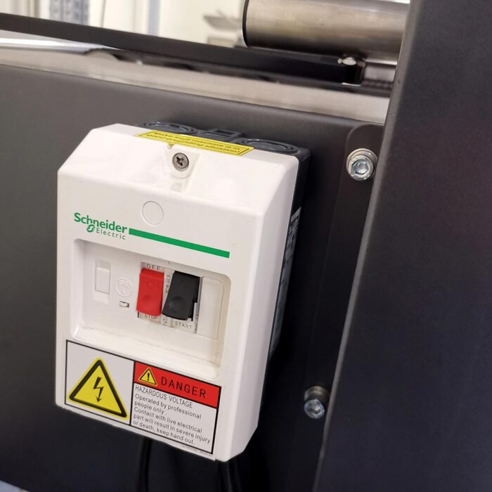Zbliżenie wyłącznika zasilania Schneider Electric z czerwoną dźwignią OFF i czarną dźwignią ON, etykietami ostrzegawczymi i znakiem wysokiego napięcia, zamontowanego na sprzęcie przemysłowym obok Półautomatycznej zaklejarki Easy Tape 50 TBB.