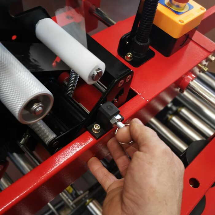 Ręka przekręca klucz w przełączniku na półautomatycznej zaklejarce Easy Tape 50 SB, przemysłowej maszynie z widocznymi rolkami i przyciskami sterującymi.