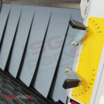 Zbliżenie na przemysłową maszynę pakującą Tunel Obkurczający S 85 DC z dwiema czarnymi dźwigniami, żółtym wskaźnikiem pomiarowym, metalowymi klapami i logo ISG Pack w tle.