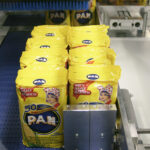 Żółte worki z białą mąką kukurydzianą PAN przesuwają się wzdłuż przenośnika taśmowego w fabryce, mijając Automatyczną zgrzewarkę do zgrzewek FA800AR-150Z. Opakowanie z twarzą kobiety i napisem "50 lat tradycji" jest gotowe do dystrybucji.