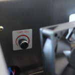 Zbliżenie pokrętła TEMP. ADJ. z numerami 1-5 na Półautomatyczna bandownica stołowa Eco Strap 501, z częściowo widocznym i nieco nieostrym wentylatorem chłodzącym na pierwszym planie.