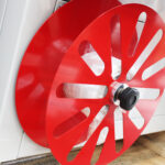 Zbliżenie czerwonej metalowej rolki z dużymi wycięciami i czarnym pokrętłem, zamontowanej na Automatycznej zgrzewarce kątowej do folii Matic Sealer 65 E, trzymającej przezroczystą folię. W tle widoczna jest biała obudowa maszyny.