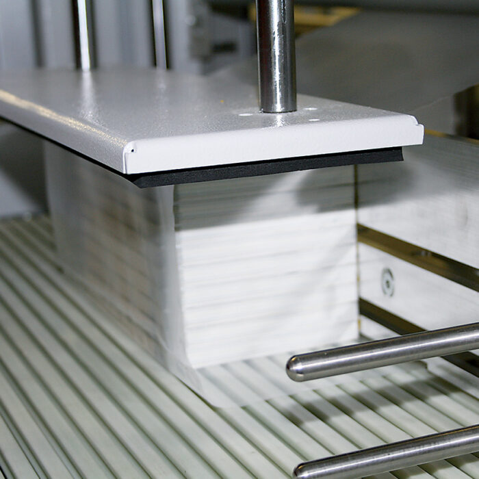 Zbliżenie stosu białego papieru trzymanego przez metalową i plastikową część wewnątrz Automatycznej zgrzewarki do zgrzewek FA802AR 230R.