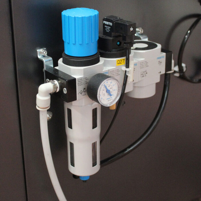 Zbliżenie zespołu pneumatycznego filtra powietrza i regulatora Festo używanego w Automatycznej Formierce Robo Former 50 SB, pokazujące niebieskie pokrętło regulacji, manometr i czarno-białe złącza na metalowym wsporniku.