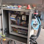 Otwarty panel sterowania elektrycznego ze stali nierdzewnej do automatycznej zaklejarki Auto Tape 50 CF SS, wyposażony w różne przewody, przekaźniki, wyłączniki automatyczne i czerwony wyłącznik awaryjny.