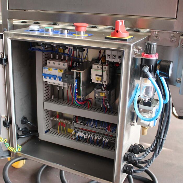 Otwarty panel sterowania elektrycznego ze stali nierdzewnej do automatycznej zaklejarki Auto Tape 50 CF SS, wyposażony w różne przewody, przekaźniki, wyłączniki automatyczne i czerwony wyłącznik awaryjny.