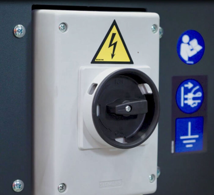Zbliżenie przełącznika elektrycznego ze znakiem ostrzegawczym wysokiego napięcia i niebieskimi symbolami bezpieczeństwa, takimi jak instrukcje uziemienia, jest pokazane obok Półautomatyczna zaklejarka kartonów X5 - SIAT.