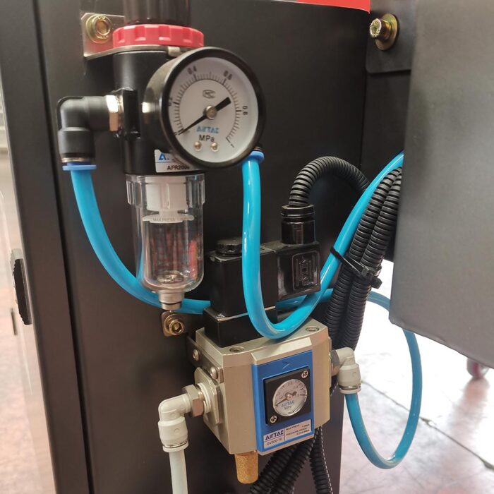 Zbliżenie regulatora ciśnienia powietrza z manometrem (w MPa), filtrem, niebieską rurką oraz połączeniami elektrycznymi i pneumatycznymi na Automatycznej zaklejarce Auto Tape 50 CF.
