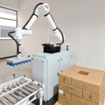 Robot kolaboracyjny Easy-PAL 620-1650F z przyssawkami jest umieszczony w pobliżu przenośnika taśmowego i kilku kartonów w czystym, nowoczesnym otoczeniu przemysłowym.