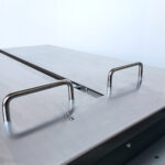 Zbliżenie metalowej powierzchni Półautomatycznej bandownicy stołowej Eco Strap 501L pokazuje dwa metalowe uchwyty w kształcie litery U i centralny szew, a wszystko to na jednolitym jasnym tle.