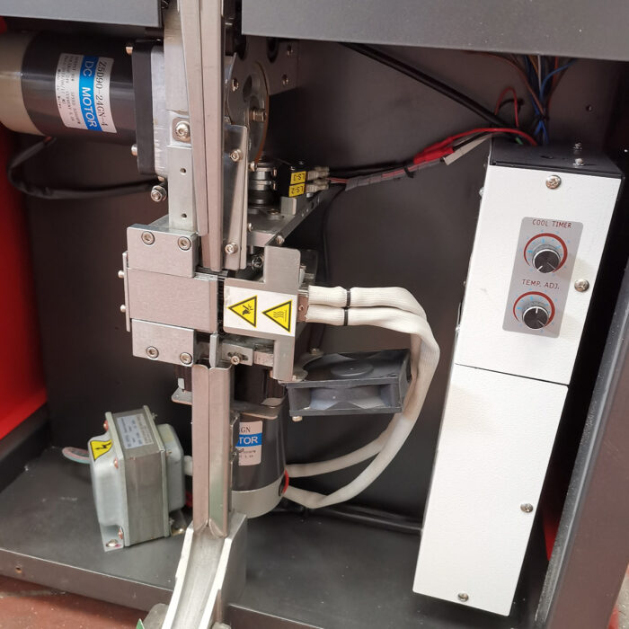 Zbliżenie Półautomatyczna bandownica do palet Pallet Strap T45, pokazująca silniki, okablowanie, części metalowe, etykiety ostrzegawcze i panel sterowania z Cool Timer i Temp. Adj., umieszczony w typowej metalowej obudowie.