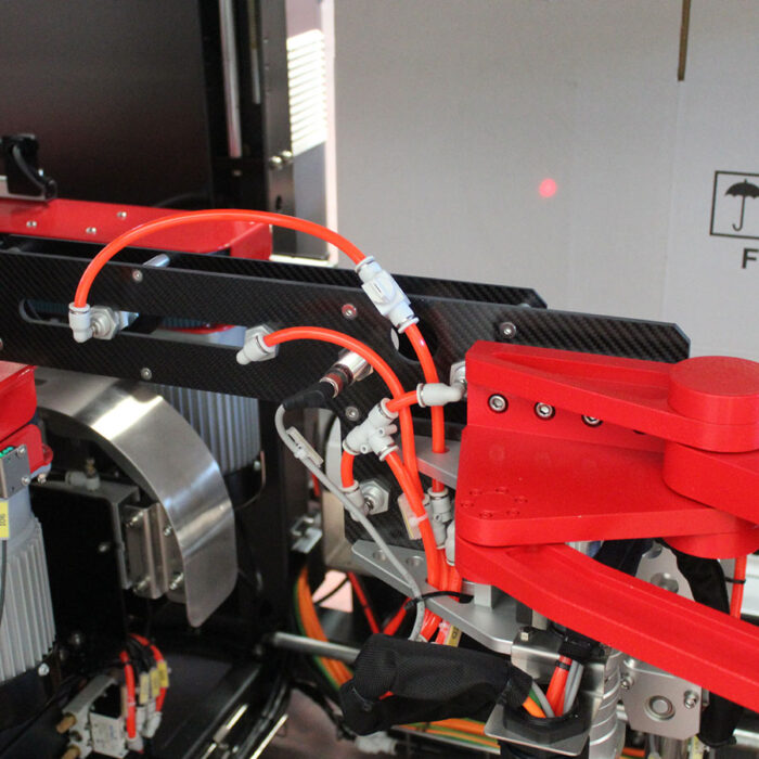 Zbliżenie Automatycznej formierki Robo Former 50 SB z czerwonymi ramionami robota, pomarańczowymi kablami i szczegółowymi elementami mechanicznymi, z częściowo widocznym znakiem ostrzegawczym w tle.