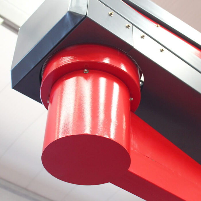 Zbliżenie czerwono-szarego elementu z palety Owijarka ramieniowa Rotary Wrap 2300 B, z cylindryczną sekcją, śrubami i gładkimi metalowymi powierzchniami na rozmytym tle wnętrza.