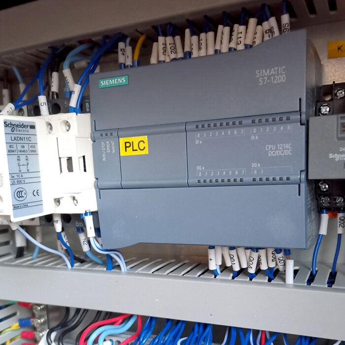 Zbliżenie na przemysłowy panel sterowania ze sterownikiem Siemens SIMATIC S7-1200 PLC, Schneider Electric LADN11C i schludnym niebiesko-białym okablowaniem - typowym dla zautomatyzowanych systemów Bandownica ramowa wiązarka PP Easy Strap 309BP/312BP.