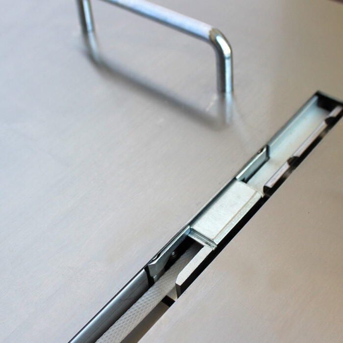 Zbliżenie metalowej powierzchni z uchwytem i wąską szczeliną zawierającą przesuwane metalowe części, prawdopodobnie część mechanizmu blokującego w Półautomatycznej bandownicy stołowej Eco Strap 501.