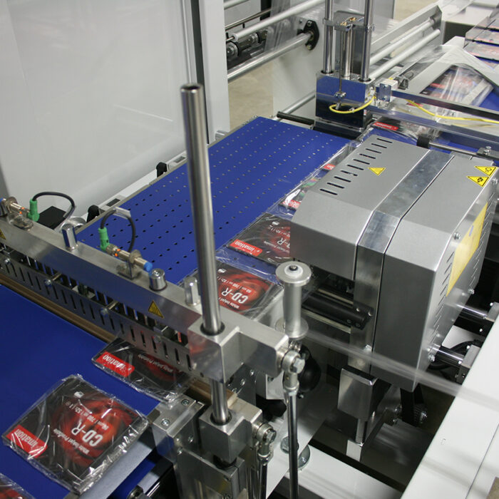 Automatyczna zgrzewarka kątowa Ultra Sealer 70 HSS owija zestawy masek CPR w przezroczystą folię na taśmie produkcyjnej, układając je obok siebie do dalszego przetwarzania lub wysyłki.
