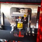 Zbliżenie na Automatyczną zaklejarkę Matic Tape 50 CF HM, pokazujące jej metalowe elementy, rury, widoczny wskaźnik i żółty znak ostrzegawczy gorącej powierzchni.