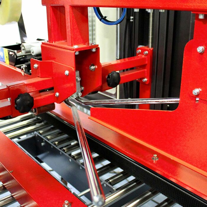 Zbliżenie na Automatyczną zaklejarkę Auto Tape 50 HM, czerwoną automatyczną maszynę pakującą z metalowymi ramionami i rolkami, przeznaczoną do zaklejania produktów na przenośniku.