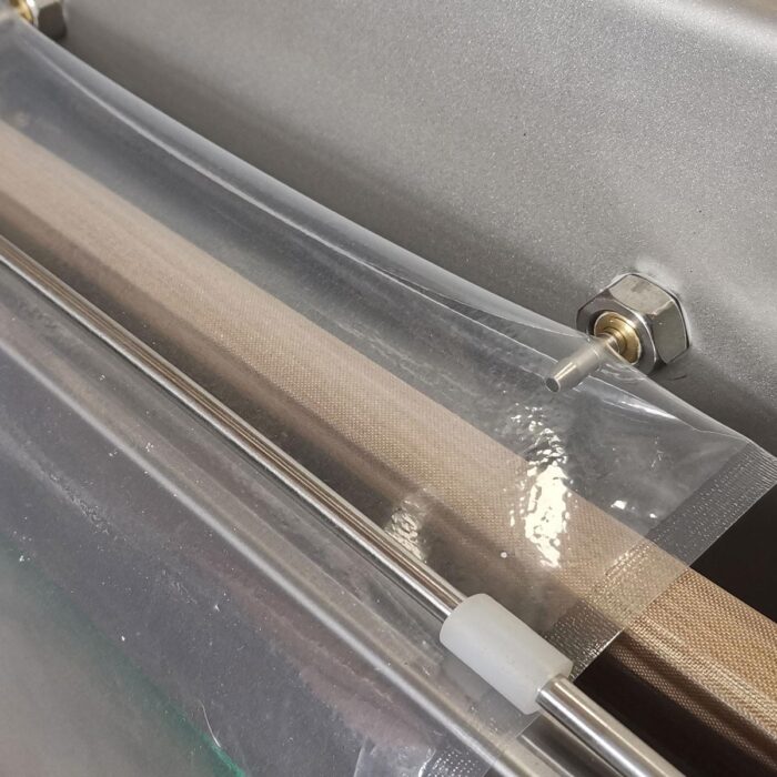 Zbliżenie plastikowej torby zgrzewanej termicznie przez Komorową pakowarkę próżniową Eco Vac 300S TB, pokazujące taśmę zgrzewającą, metalowe pręty i część torby gotową do zgrzania.