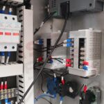 Zbliżenie panelu sterowania elektrycznego w metalowej obudowie dla Pionowa maszyna pakująca Mini Vert 240 PP, prezentująca uporządkowane przekaźniki, wyłączniki i złącza z okablowaniem urządzenia.