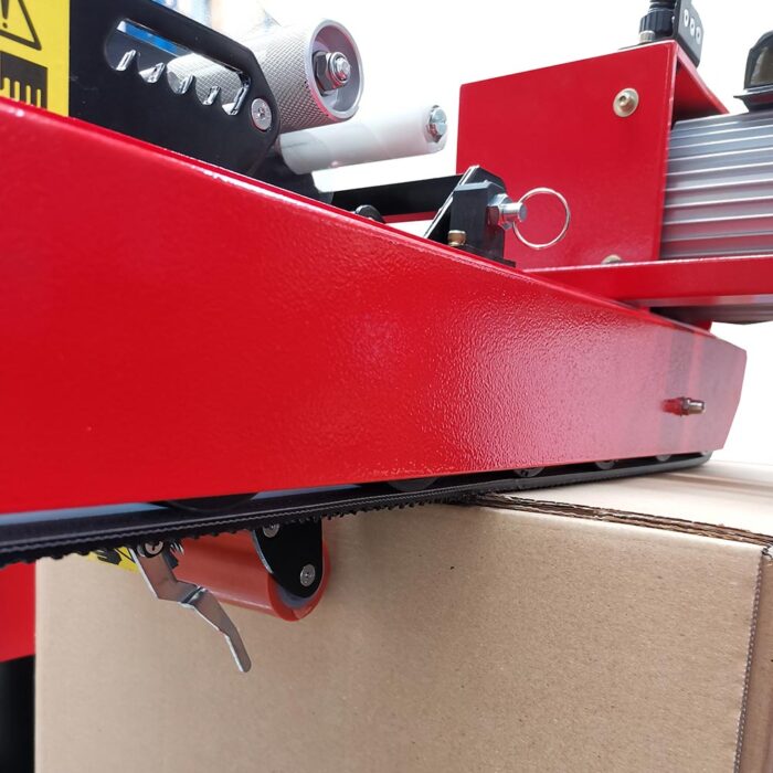 Zbliżenie na Półautomatyczną zaklejarkę Easy Tape 70 TSB zaklejającą kartonowe pudełko. Przenośnik taśmowy, mechanizm dźwigniowy i metalowe rolki są pokazane szczegółowo, a inne części maszyny są widoczne w tle.